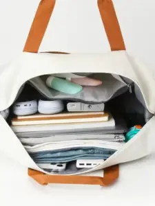 తెల్లటి ట్రావెల్ బ్యాగ్ యొక్క ముందరి దృశ్యం దాని సొగసైన డిజైన్ మరియు ముందు జేబును చూపుతుంది