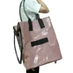 Taong nagdadala ng isang malaking gulong na PP na pinagtagpi ng pamimili ng tote na may siper -., makintab na kulay rosas na may itim na hawakan at gulong - show mula sa gilid, Perpekto para sa pag -highlight ng OEM ODM Design Versatility.