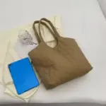Unha bolsa acolchada acolchada para mulleres en marrón, unha tableta azul, e colócanse un vaso claro sobre un fondo de pano de crema.