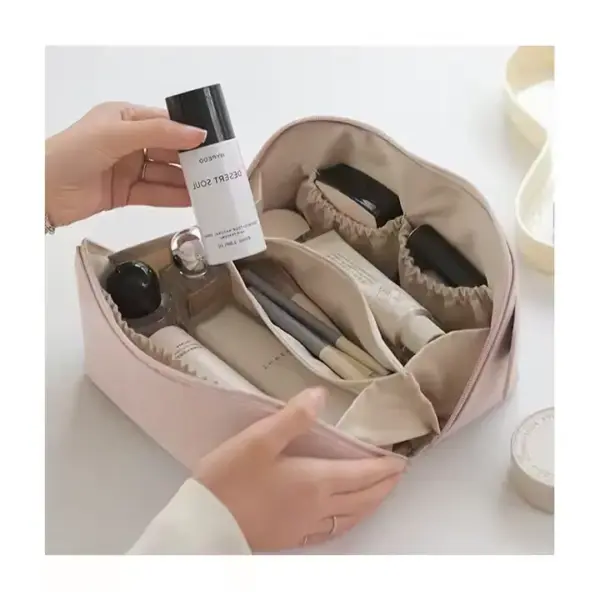 Mga kamot nga naggunit sa usa ka botelya sa ibabaw sa usa ka bukas nga Beige Portable Waterproof Zippered makoup bag nga puno sa mga produkto sa Skincare ug makeup.