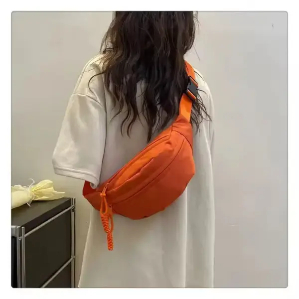 Egy személy, Ellátva a kamerától, Állítható, sportos kereszttest táskát visel narancssárgában egy laza fehér póló felett.