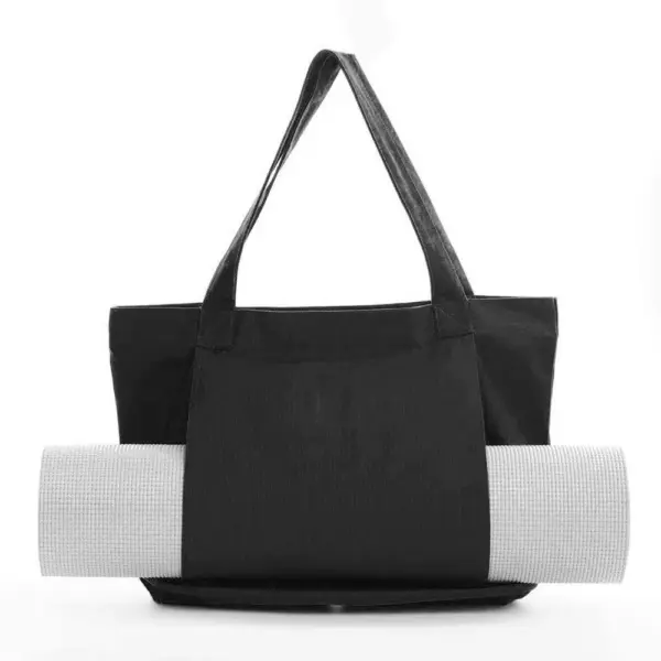 Women's Yoga Fitness Tote with shoulder straps, Zobrazeno černou, drží ve své přední kapse na bílém pozadí rohož jógy.