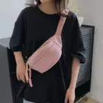 Pessoa vestindo uma camiseta preta solta e uma bolsa crossbody esportiva ajustável em rosa claro, em pé dentro de casa, destacando moda ODM da moda.