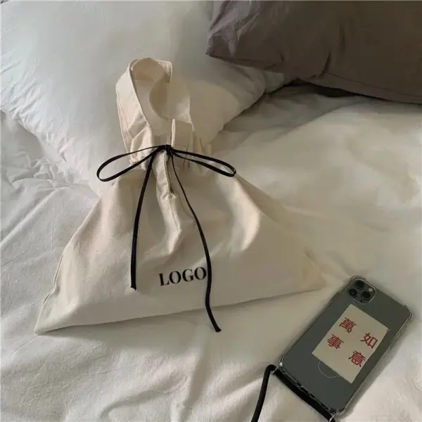 മിനിമലിസ്റ്റ് ക്യാൻവാസ് ഡ്രോസ്ട്രിംഗ് സ്ത്രീകൾക്ക്, labeled "LOGO," ODM / OM ഇഷ്ടാനുസൃതമാക്കലിന് അനുയോജ്യം, ഒരു ചൈനീസ് ടെക്സ്റ്റ് കേസ് ഉപയോഗിച്ച് ഒരു ഫോണിനടുത്തുള്ള ഒരു കട്ടിലിൽ ഇരിക്കുന്നു.