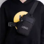 Osoba v černé mikině s smajlíkem, nosit minimalistickou nastavitelnou tašku Crossbody. Ideální pro přizpůsobení OEM/ODM.