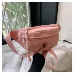 Uma mão segura uma bolsa esportiva ajustável em rosa claro com um zíper trançado puxe perto de uma janela com plantas frondosas do lado de fora.