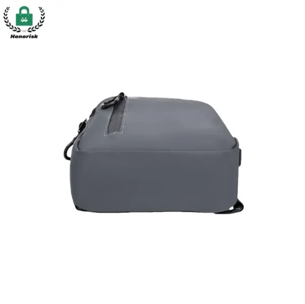 Pelēkas taisnstūrveida ūdensnecaurlaidīgas krusteniskās ķermeņa soma ārpus telpām, Parādīts no sāniem ar rāvējslēdzēju un augšējo siksnu redzamu.