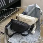 Duas sacolas esportivas ajustáveis, um preto e um branco, são exibidos em uma jaqueta jeans em um carrinho de compras de metal.