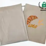 બે ન રંગેલું .ની કાપડ સુતરાઉ બ્રેડ ડ્રોસ્ટિંગ શોપિંગ બેગ; એકમાં ક્રોસન્ટ હોય છે, ઘઉં, and "LOGO" છાપું, OEM/ODM વિકલ્પો પ્રકાશિત. માનક લોગો ઉપર જમણી બાજુ દેખાય છે.